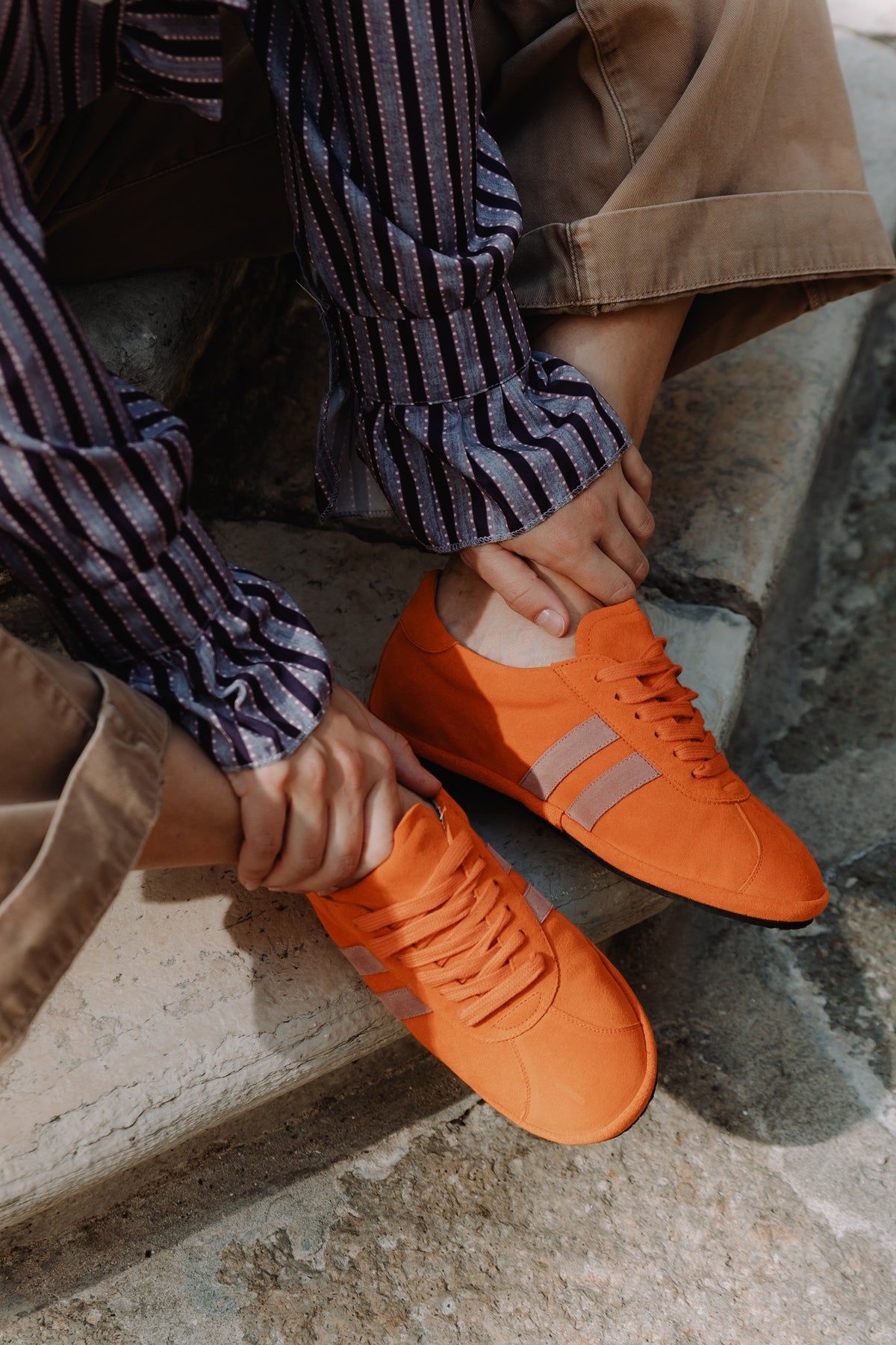 A close-up lifestyle shot: An orange suede sneaker with pink stripes and matching laces, worn by model detail
