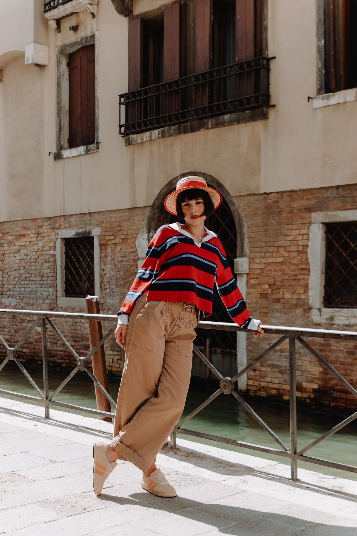 A beige suede gondolina sneaker with two vertical peach-orange stripes on the side, matching beige laces, worn by model