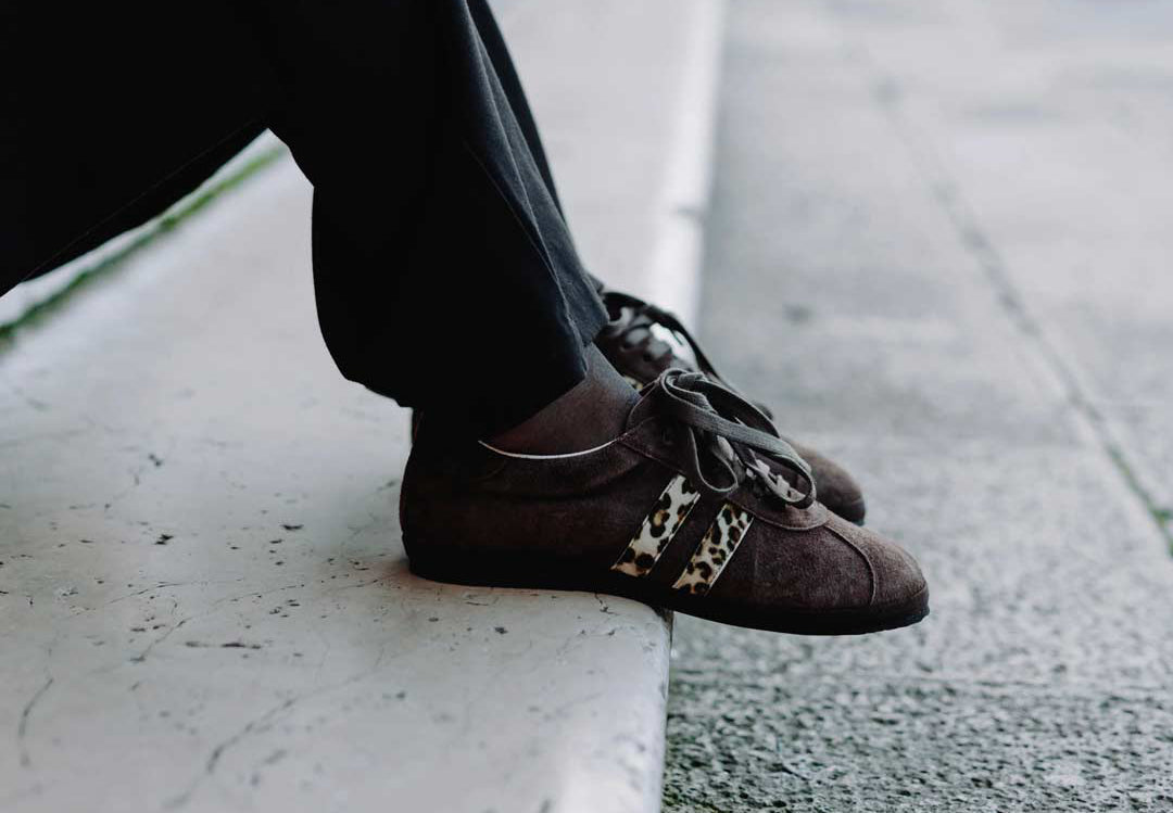 Sneakers gondolina marroni con dettaglio leopardato sui lati, indossate da una modella seduta sulle scale.