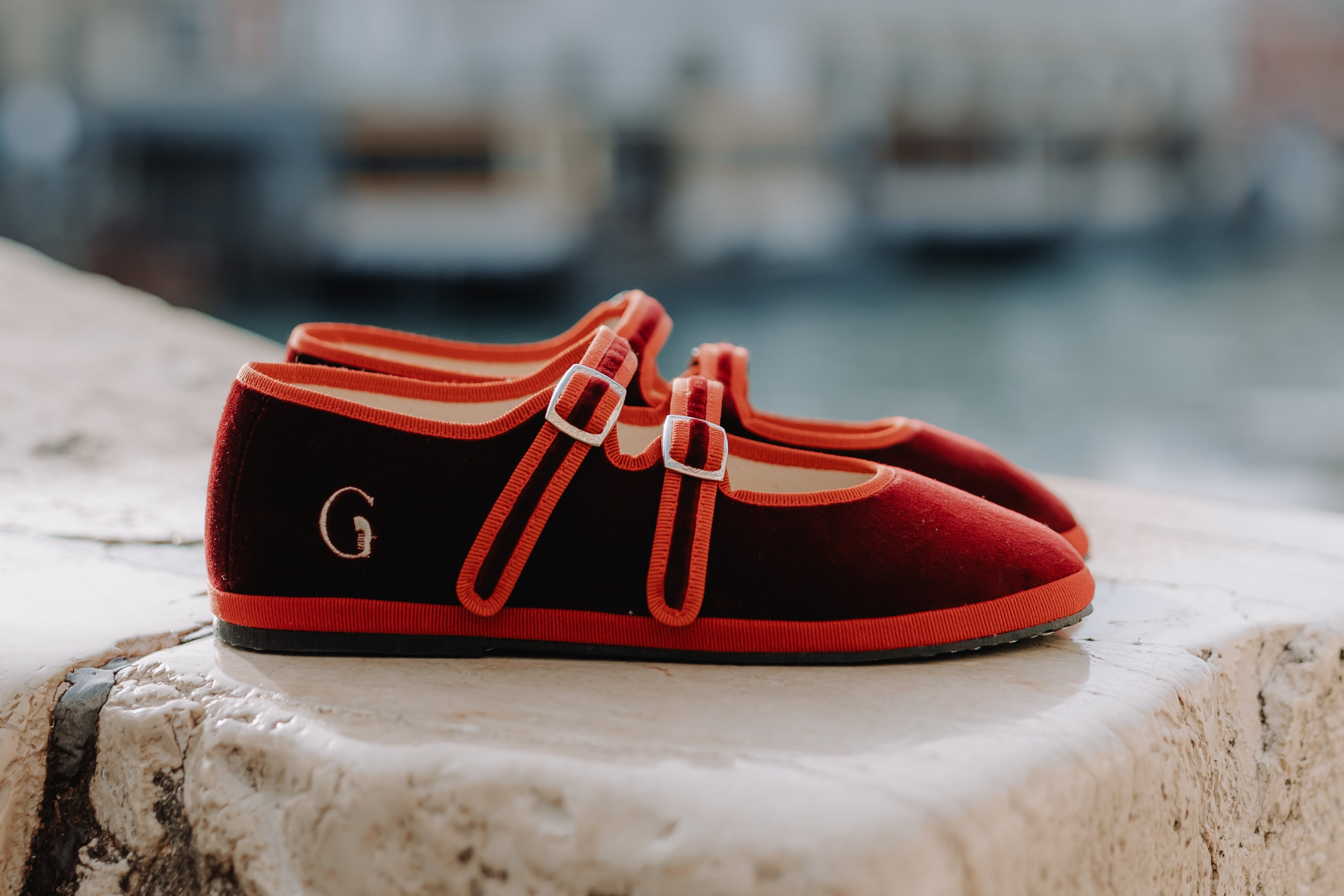Red and black shoes with a logo on a stone ledge with a blurred cityscape in the background