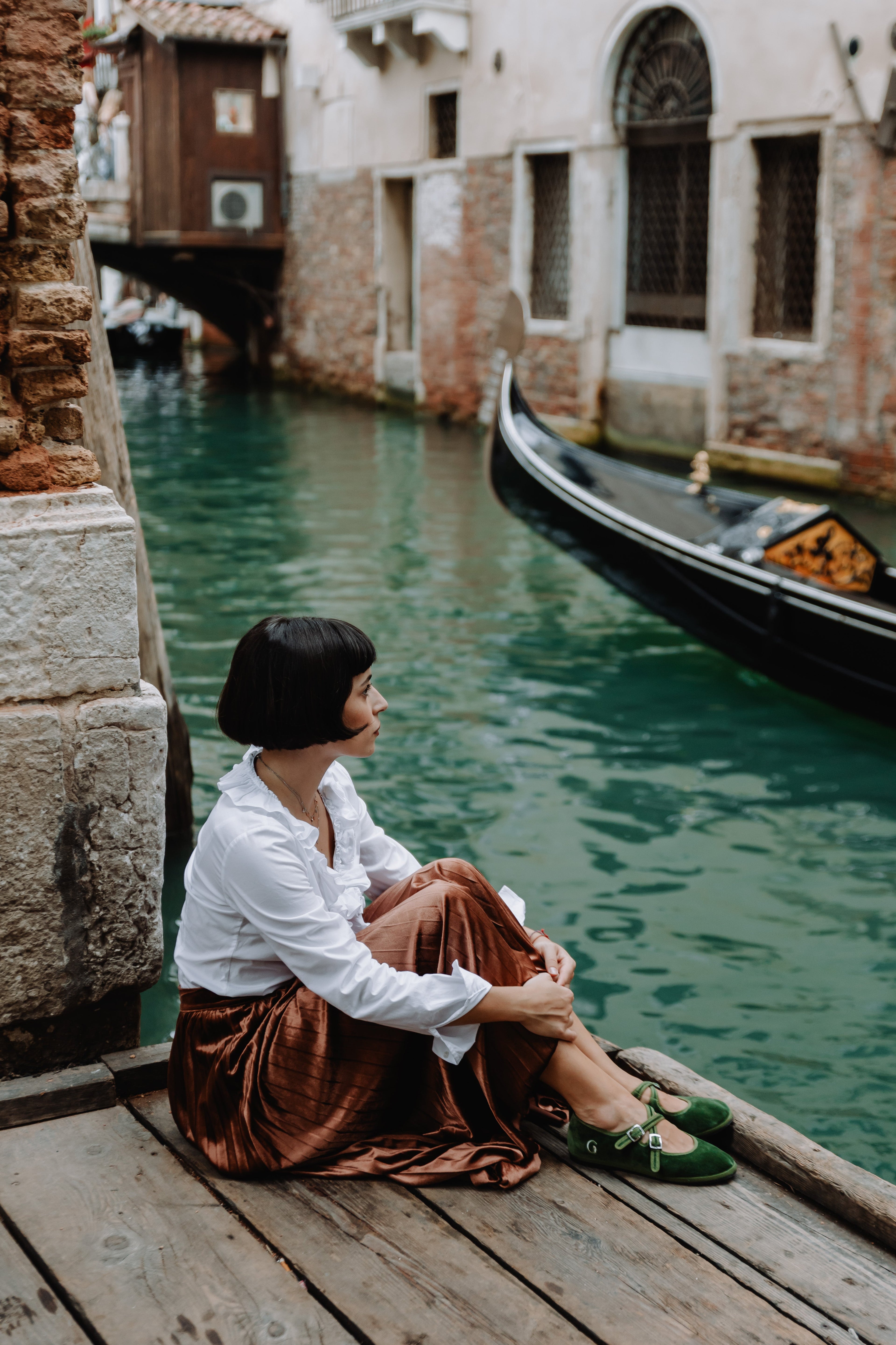Woman sitting by a canal with a gondola in the background
